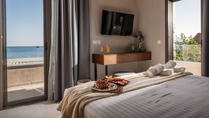 A hotel room with a bed, a TV, a desk, and a view of the beach.