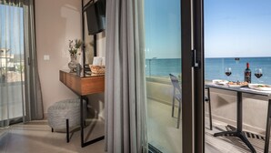 A balcony with a table set for dining, a TV mounted on the wall, and a view of the sea.