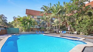 A swimming pool with blue tiles, surrounded by palm trees and lounge chairs.