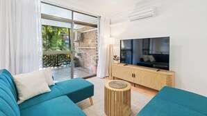 A modern living room with a large flat-screen TV, teal sofas, and a wooden sideboard.