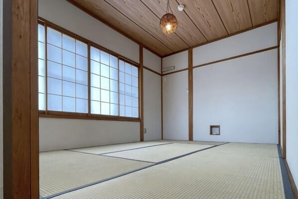 Una habitación japonesa tradicional con suelo de tatami, vigas de madera y ventanas amplias.