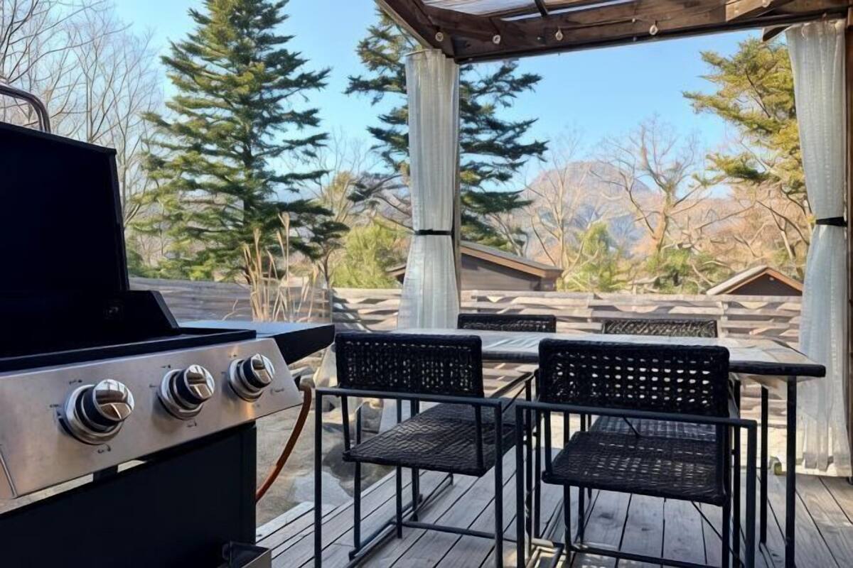 Une terrasse extérieure avec un barbecue, deux chaises et une table.