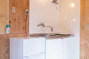 A compact kitchen with a built-in sink, a white refrigerator, and wooden paneling on the walls. - IZUKOGEN TENT RESORT (Ito)