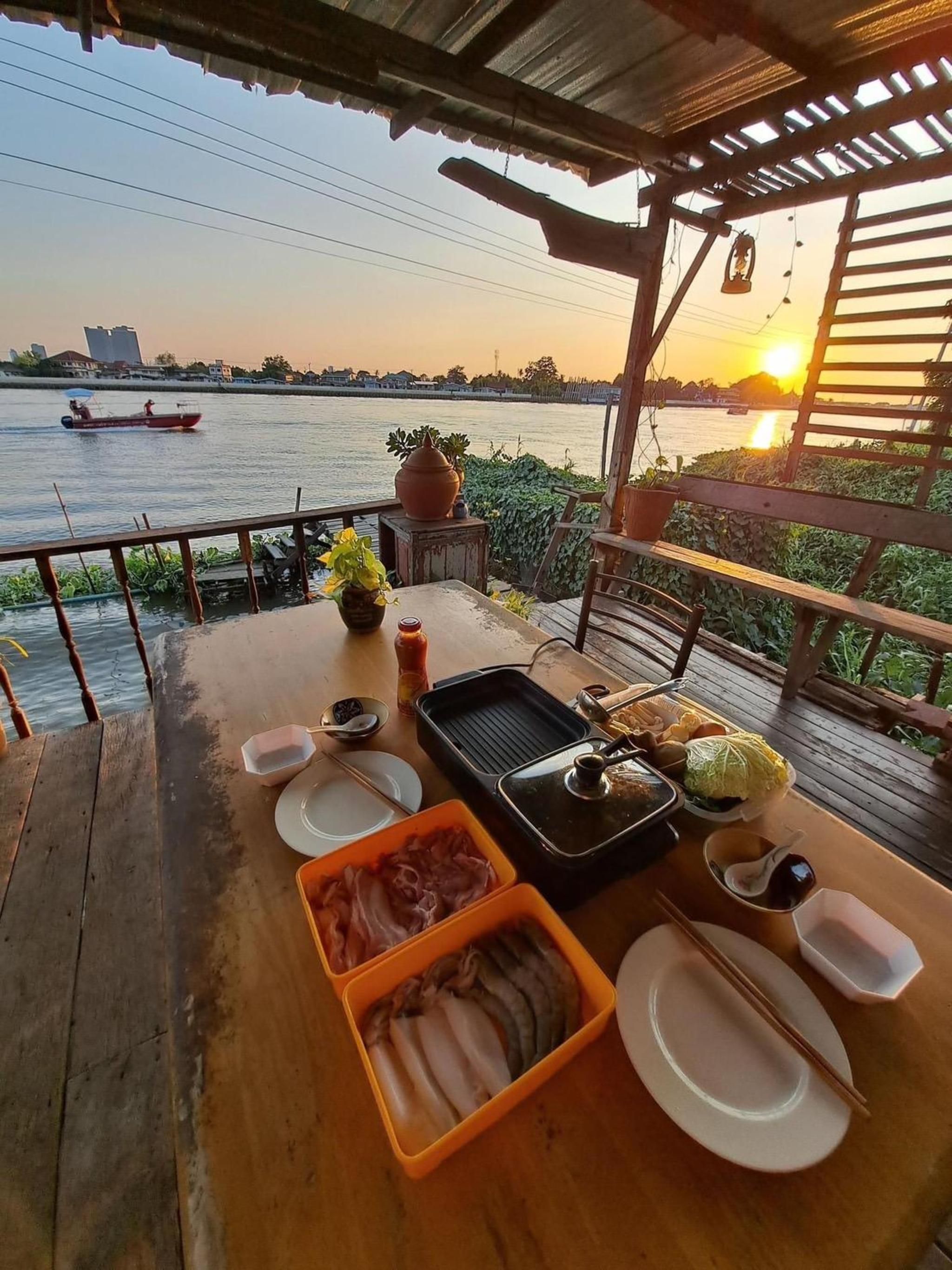 A wooden table set for dining with a river view, a grill, and a boat in the background.