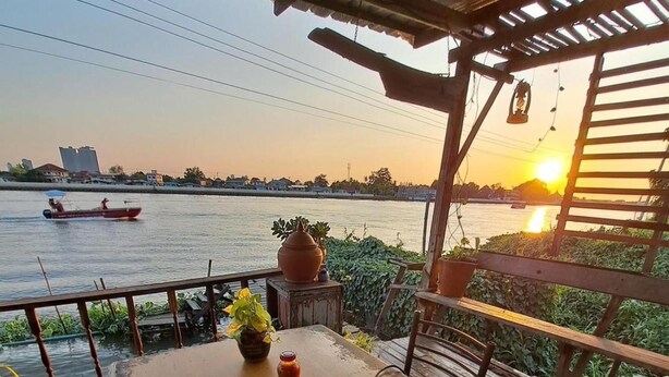 Une table en bois, dressée pour le dîner, avec vue sur la rivière, un barbecue et un bateau en arrière-plan.