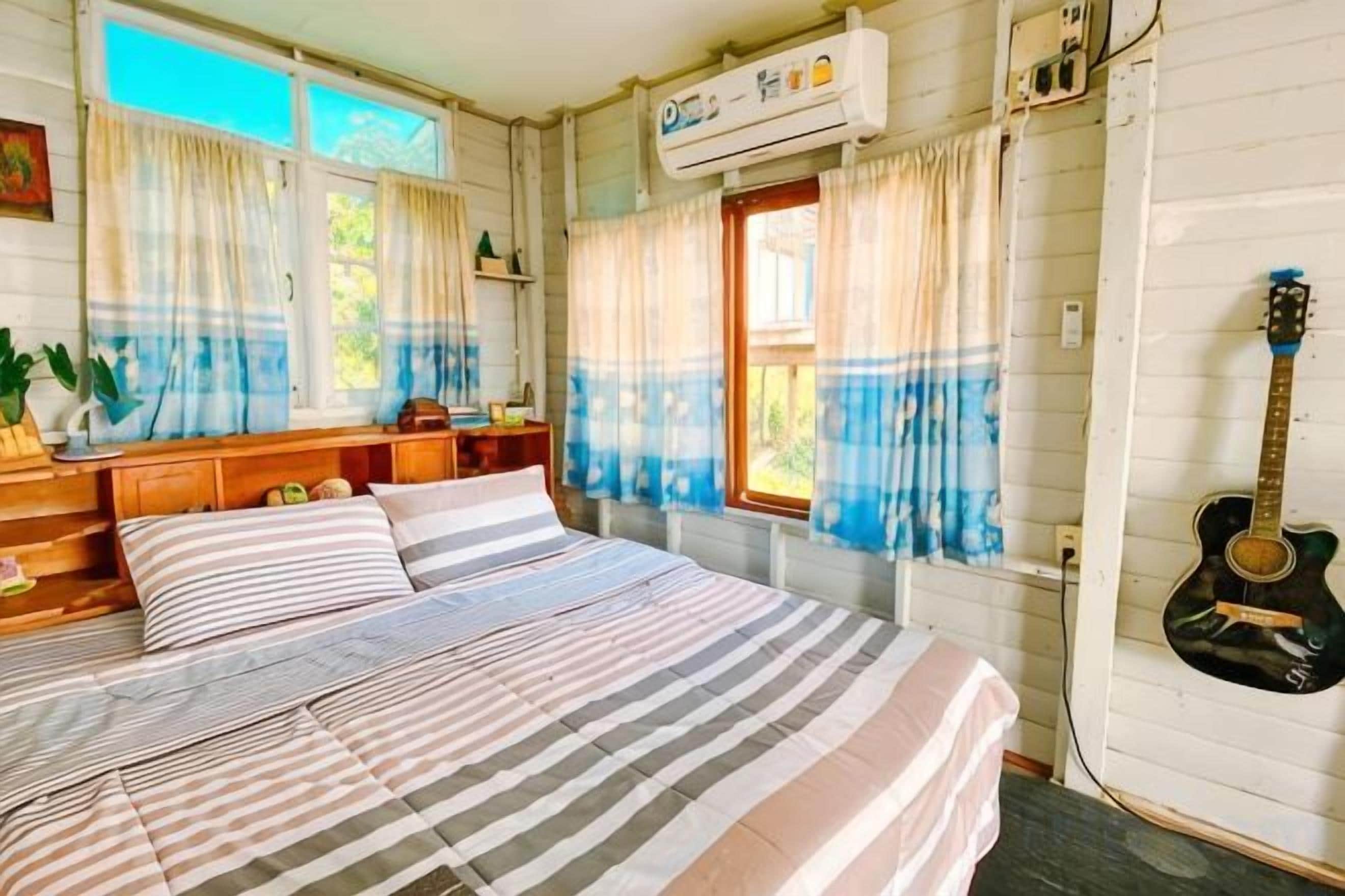 Una camera da letto con un letto, tende, una chitarra e una finestra.