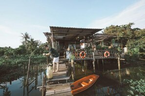 A wooden dock leading to a house with a thatched roof, surrounded by water and greenery. - Baan GoLite Ko Kret (Pak Kret)