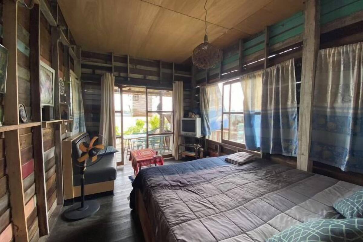 A room with a bed, a chair, a TV, and a window with curtains.