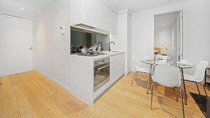 Eine moderne Küche mit weißen Schränken, einem eingebauten Backofen und einem Essbereich mit einem Glastisch und weißen Stühlen.