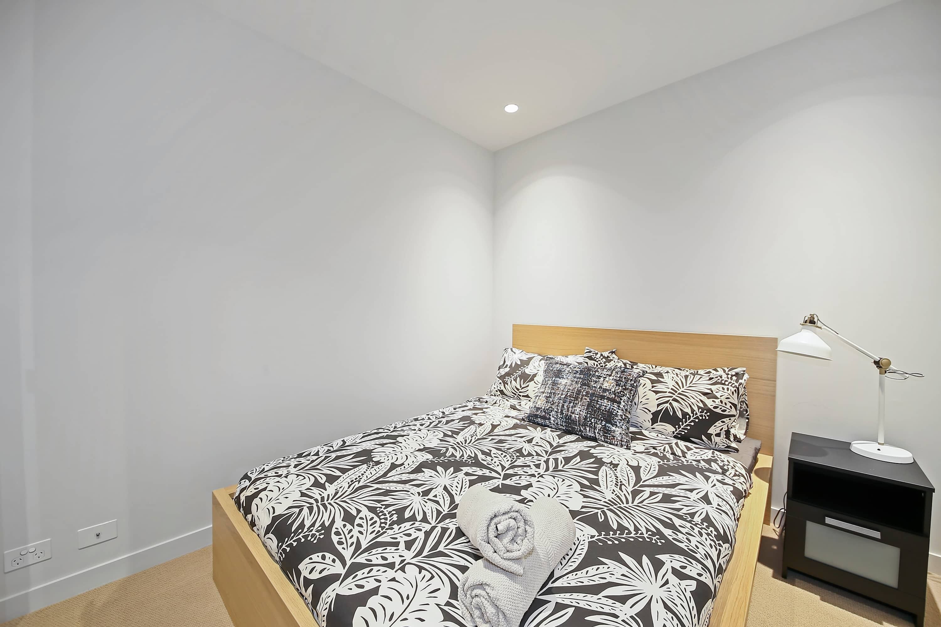 A neatly made bed with a patterned bedspread, a bedside lamp, and a nightstand.