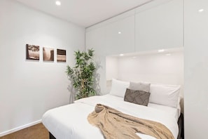 Une chambre moderne avec un grand lit, des murs blancs et trois tableaux encadrés.