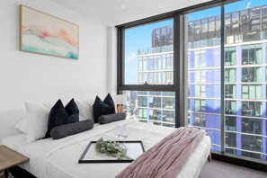 Une chambre moderne avec une grande fenêtre, un lit avec une literie blanche et une vue sur la ville.