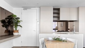 Cocina moderna con armarios blancos, una mesa de comedor de madera y sillas blancas. Hay dos plantas en macetas sobre la encimera.