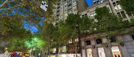 Una calle urbana de noche con un tranvía, edificios y árboles.