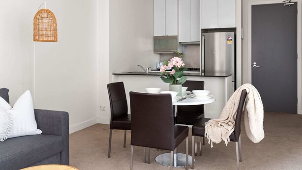 Un espace de vie compact comprenant un coin repas, une kitchenette et un canapé gris.
