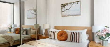 A modern hotel room with a large bed, a nightstand, a mirror, and two wall-mounted lamps.