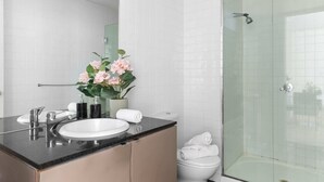 Une salle de bain moderne avec un lavabo blanc, une douche en verre et un vase rempli de fleurs roses posé sur le meuble-lavabo.