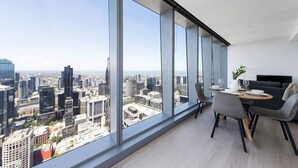 Quarto moderno com grandes janelas que oferecem vista da cidade, área de jantar com mesa e cadeiras, e um sofá.