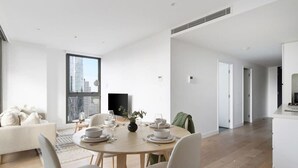 A modern living room with a dining area, a sofa, a coffee table, and a large window with a city view.