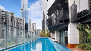 A rooftop pool with a glass barrier, surrounded by high-rise buildings.