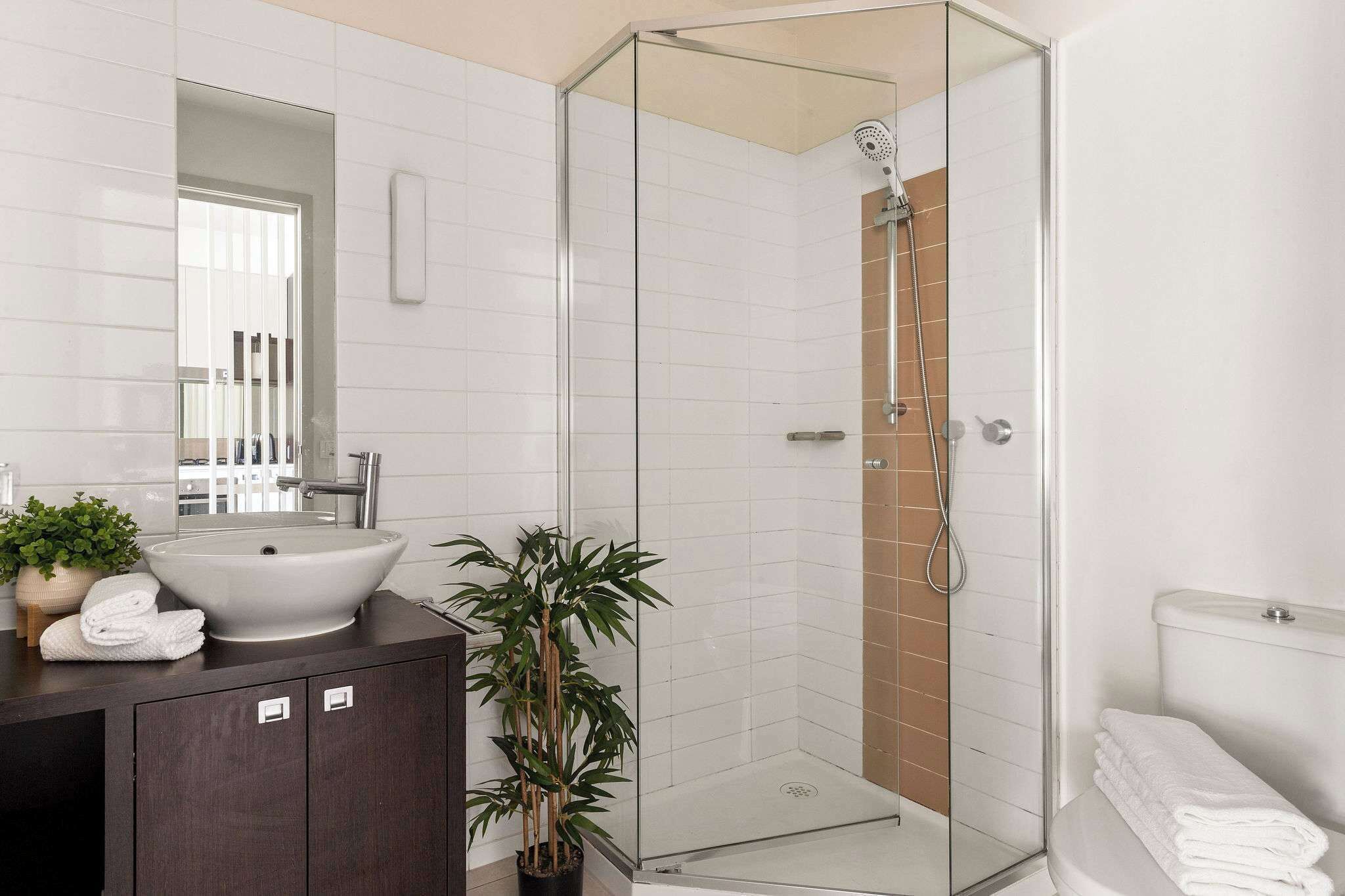 Un baño moderno con ducha envuelta en vidrio, un lavamanos grande y un mueble de tocador de madera oscura.