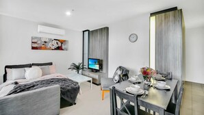 A modern hotel room with a bed, a desk, a dining table set for two, and a TV. - Comfy 2BR Apt Near Southern Cross With City Views (Melbourne)