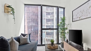 Ein modernes Wohnzimmer mit einer dunkelgrauen Couch, einem Couchtisch, einem Fernseher und einem großen Fenster mit Blick auf die Stadt.