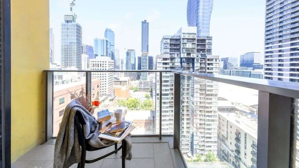 A balcony with a city view, a table with a book and a cup, and a chair with a blanket. - A Chic 2BR Apt, City Views Near Southern Cross (Melbourne)