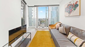Ein modernes Wohnzimmer mit einer Couch, einem gelben Teppich und einem großen Fenster mit Blick auf die Stadt.