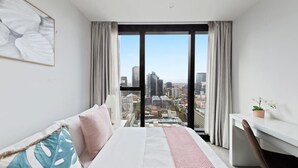 Une chambre d’hôtel moderne dotée d’un grand lit, d’un bureau et offrant une vue sur le paysage urbain grâce à de grandes fenêtres du sol au plafond.