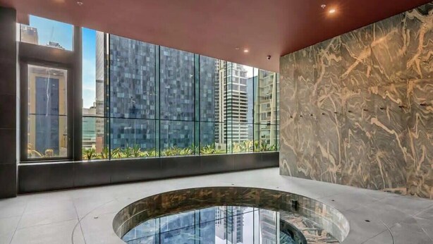 Un espace piscine intérieur moderne, doté d’une paroi vitrée, d’un mur en marbre et offrant une vue sur des immeubles de grande hauteur.