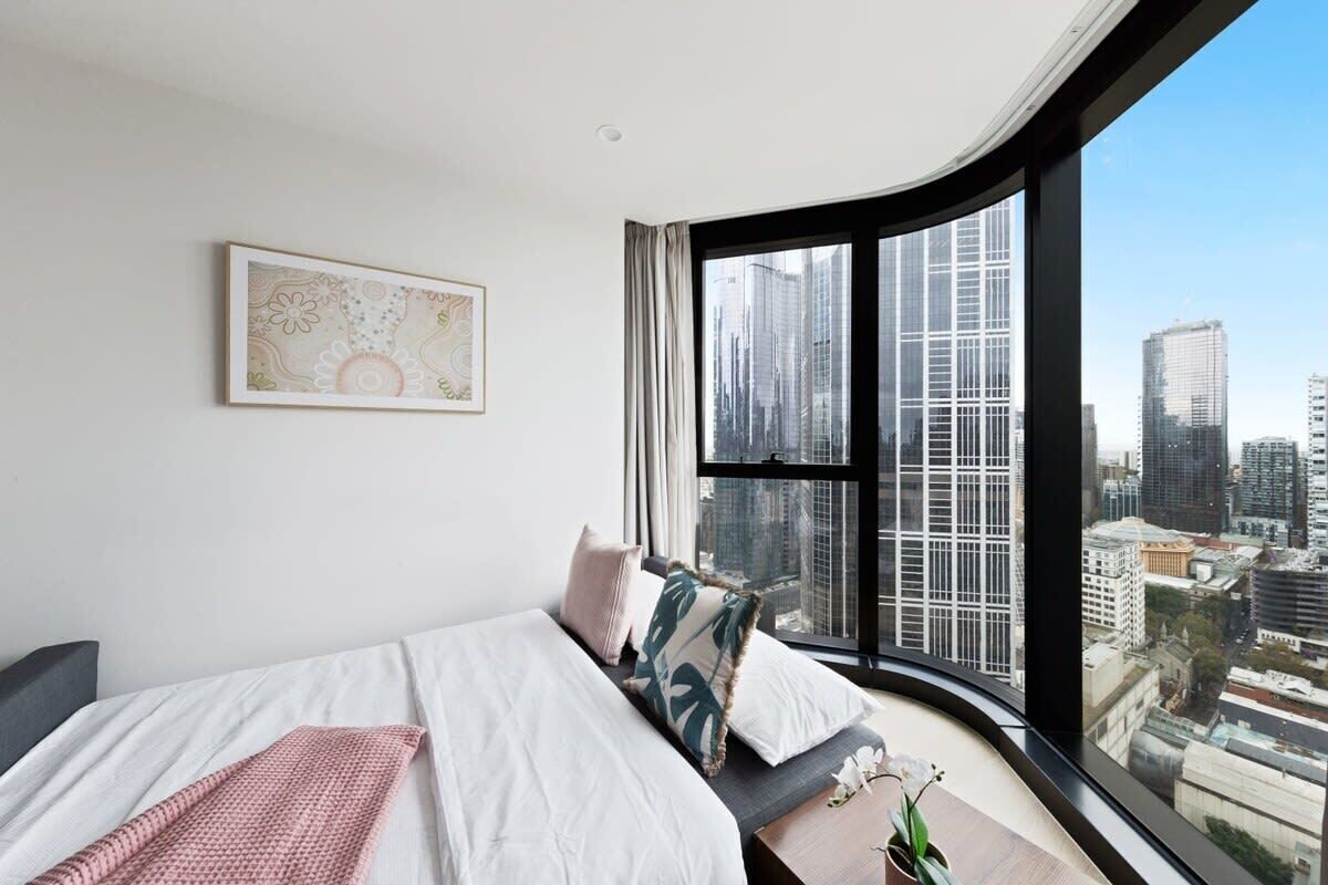 Une chambre d’hôtel moderne dotée d’une grande fenêtre donnant sur la ville, d’un lit soigneusement fait et d’une petite table agrémentée d’une plante.