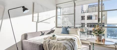 Een moderne slaapkamer met een bed, nachtkastje en een groot raam met uitzicht op de stad.