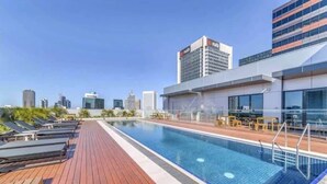 Una piscina en la azotea con tumbonas y el horizonte de la ciudad al fondo.