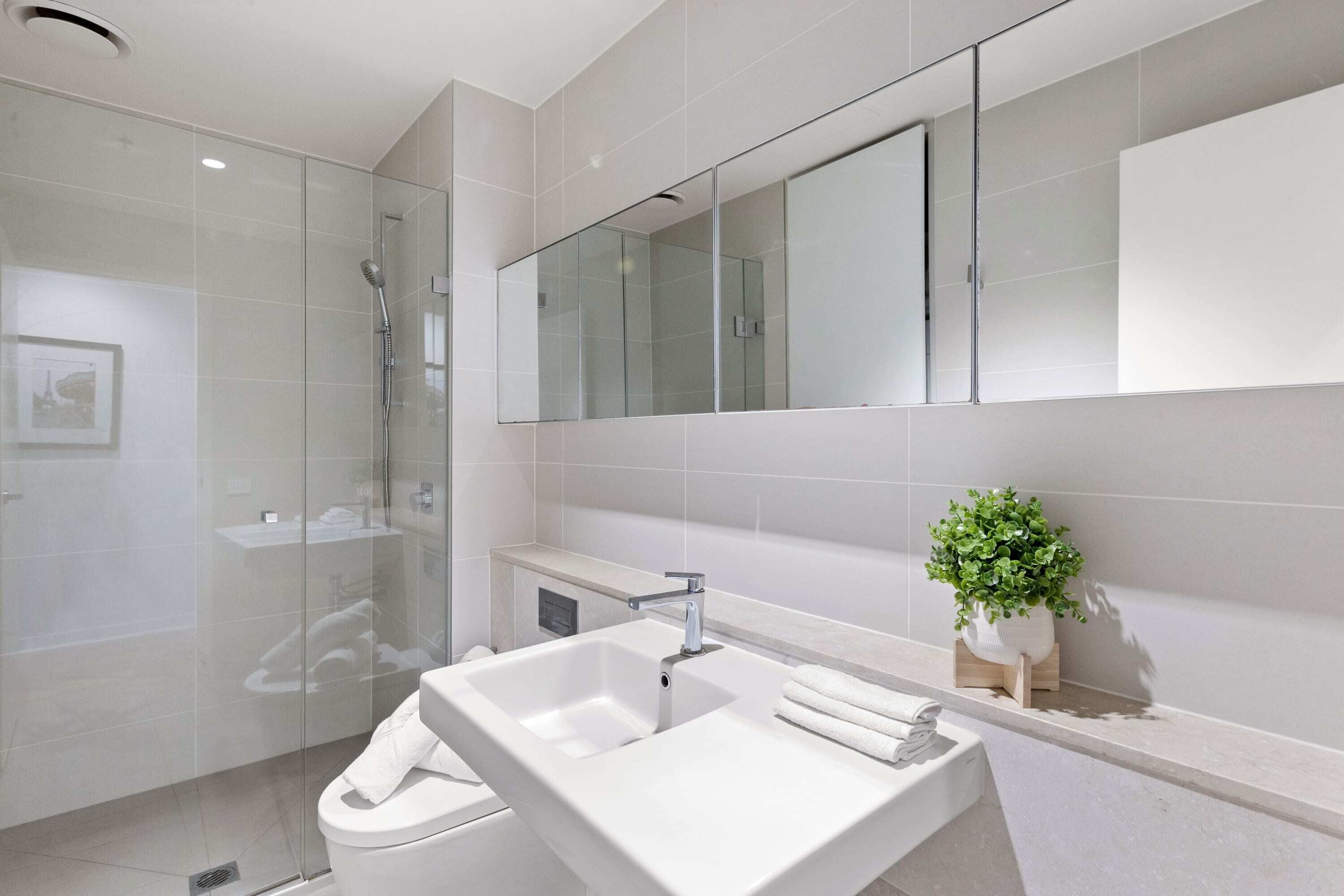 Une salle de bain moderne avec une douche à l’italienne en verre, un lavabo blanc et un grand miroir au-dessus du meuble-lavabo.