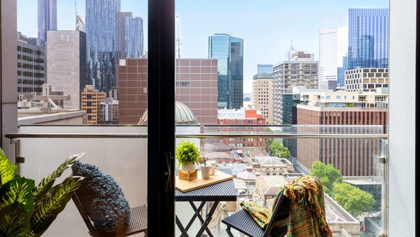 Un balcón con vista a la ciudad, una pequeña mesa con una planta y una silla.