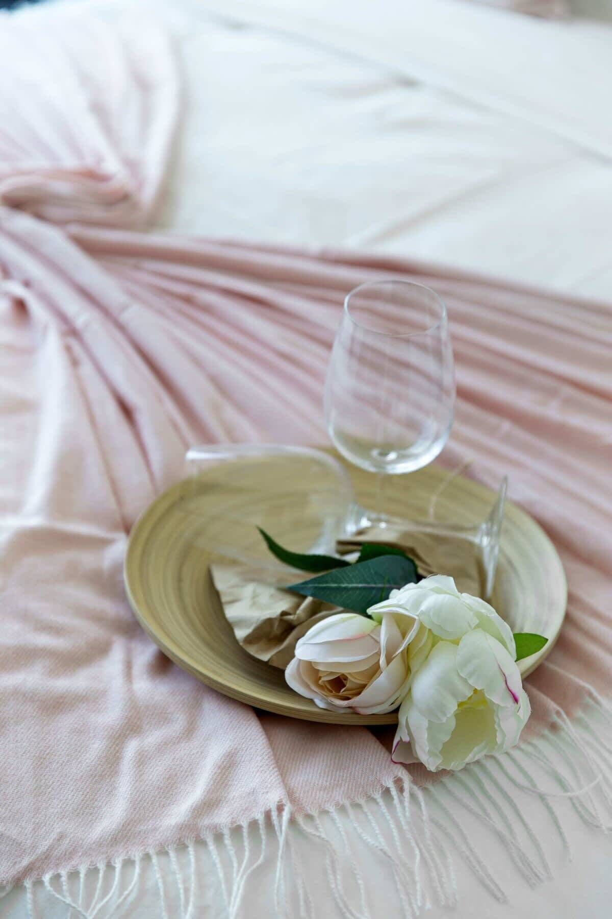 Une table dressée avec un verre, une assiette et un arrangement floral sur une nappe rose.