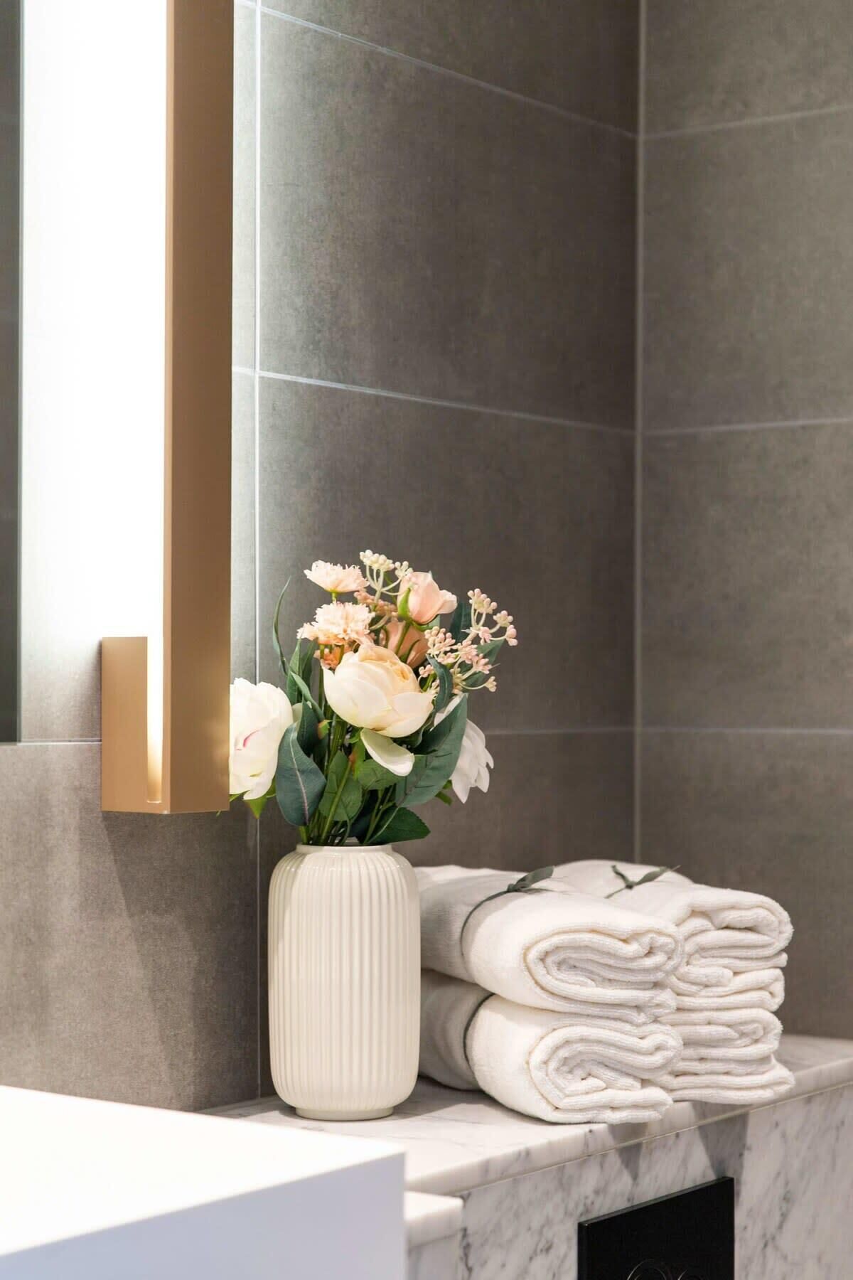 A bathroom with a marble sink, a vase of flowers, and neatly folded towels.