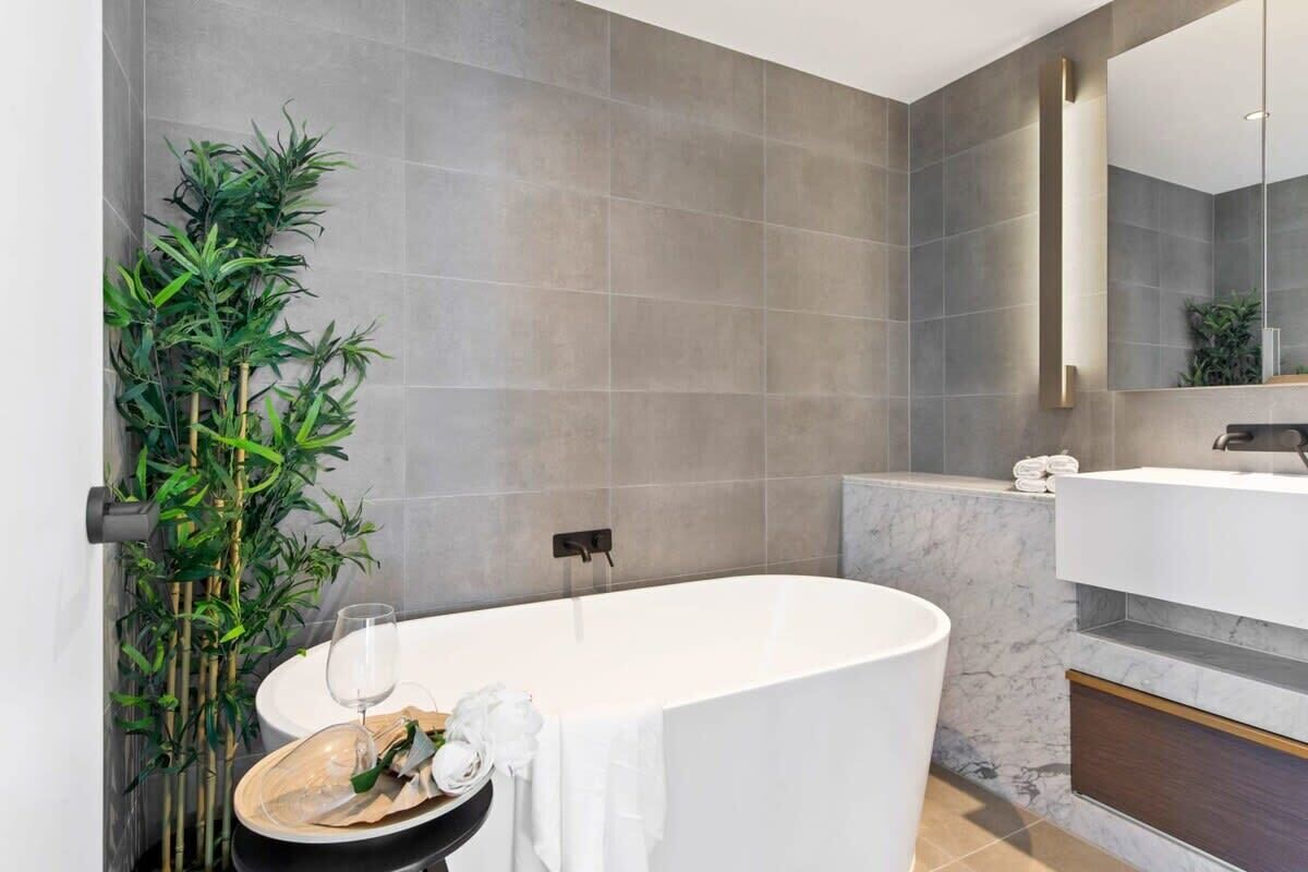 A modern bathroom with a freestanding bathtub, a large mirror, and a bamboo plant.