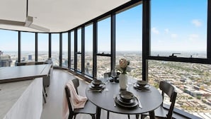 A dining area with a panoramic city view, a round table set with plates, glasses, and a vase of flowers. - Lovely 3BR Apt With Panoramic Views, Free Parking (Melbourne)
