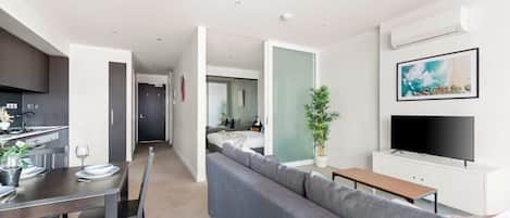 A modern apartment with a dining area, a living room with a sofa, a TV, and a kitchen.