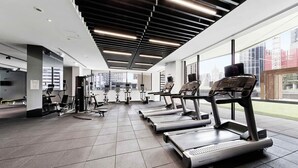 A modern gym with treadmills, weight machines, and a large window offering a city view.