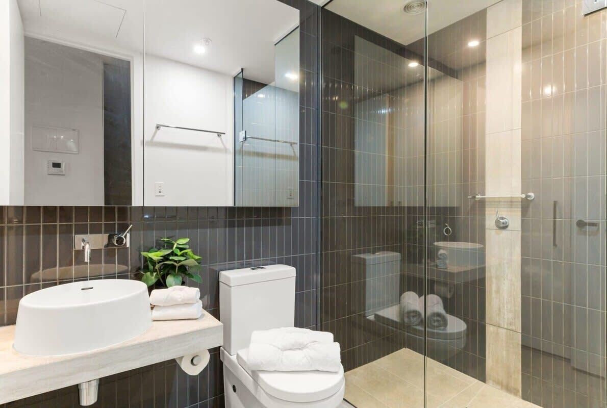 Une salle de bain moderne avec un lavabo blanc, des toilettes et une douche à parois de verre.