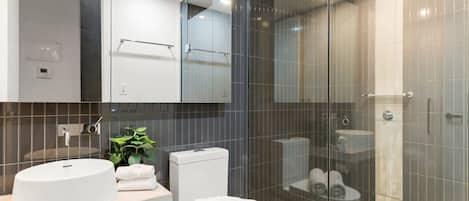 Une salle de bain moderne avec un lavabo blanc, des toilettes et une douche à parois de verre.