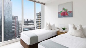 A modern hotel room with two beds, a city view, and a colorful frog painting on the wall.