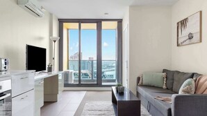A modern apartment with a kitchen, dining area, and living room. It features a large window with a city view, a flat-screen TV, and a sofa with cushions. - Southern Cross Gem: Modern Home With harbour Views (Melbourne)