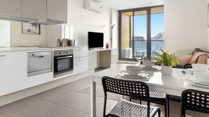 A modern kitchen with white cabinetry, a built-in oven, and a flat-screen TV. - Southern Cross Gem: Modern Home With harbour Views (Melbourne)