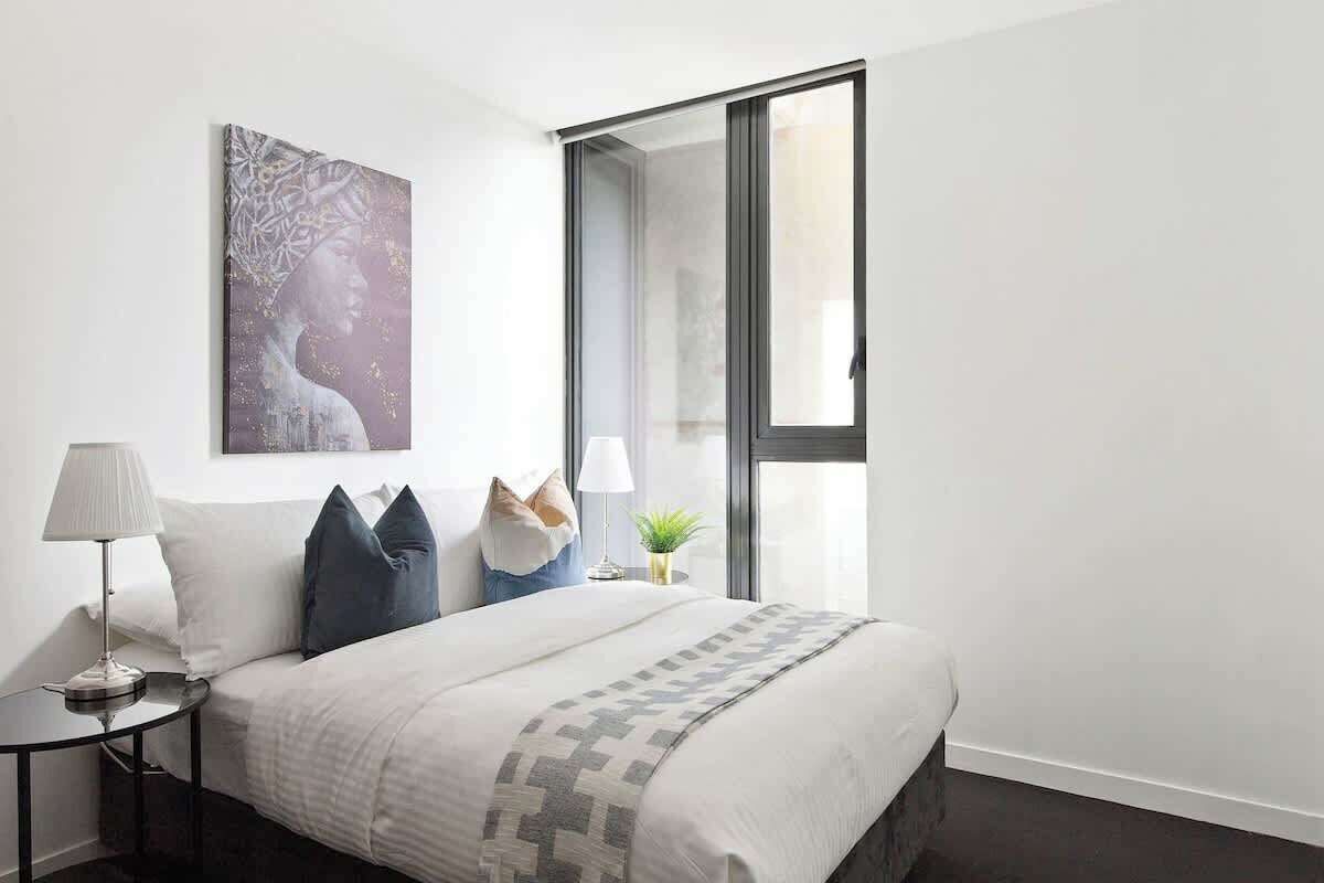 Un dormitorio moderno con una cama grande, una mesita de noche con lámpara, una obra de arte en la pared y una ventana con vistas.