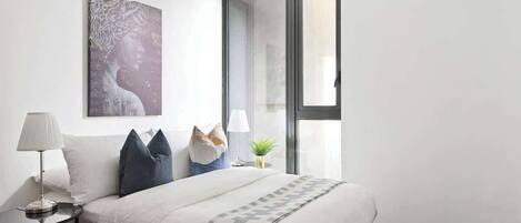 Un dormitorio moderno con una cama grande, una mesita de noche con lámpara, una obra de arte en la pared y una ventana con vistas.