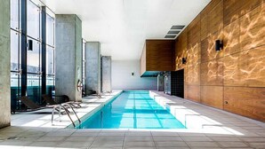 Una piscina interior moderna con agua cristalina, rodeada de sillones de descanso y amplios ventanales.